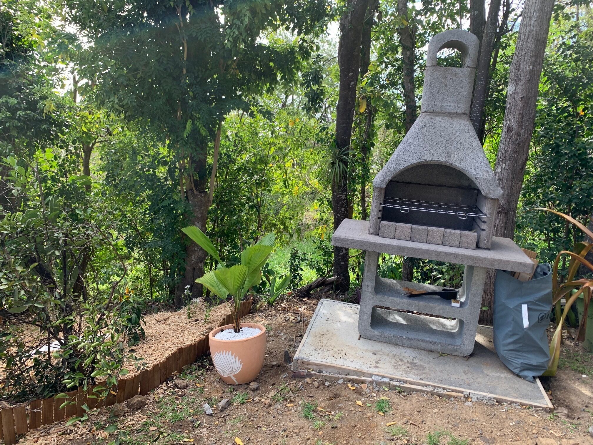 Una parrilla de piedra en un jardín, con una planta en maceta cerca.
