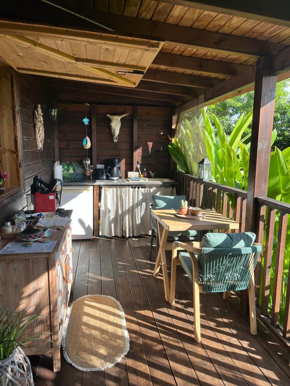 A wooden deck with a kitchen area, a dining table with chairs, and a hanging light fixture.