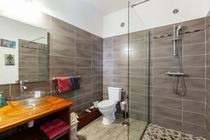 A modern bathroom with a glass sink, a toilet, and a shower area. - Gite La Tortue Bleue (Bouillante)