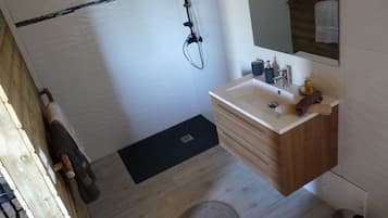 Un baño con tocador de madera, un espejo, un lavabo y una ducha.