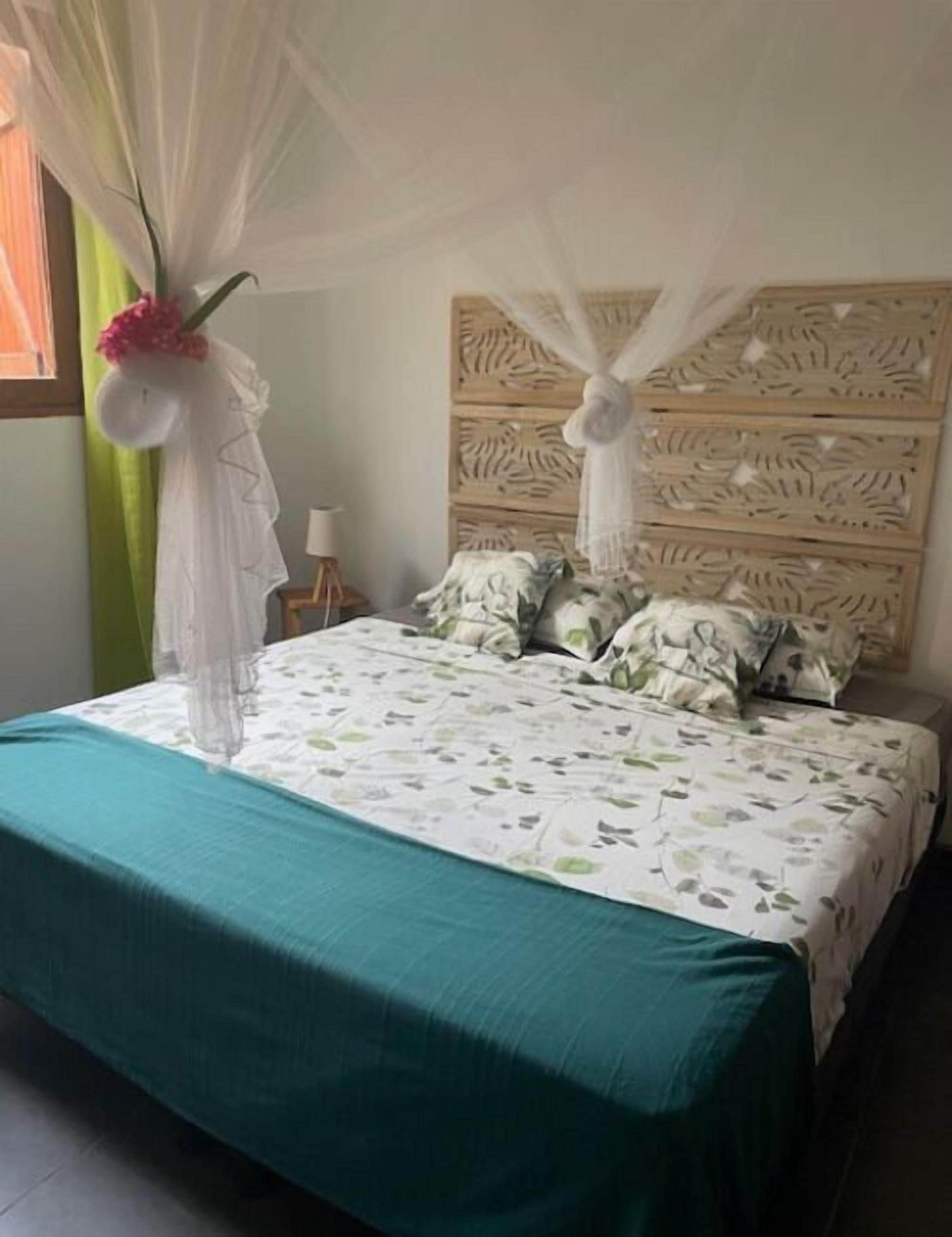 A bed with a floral bedspread, a teal bed skirt, and a canopy with white fabric and pink flowers.