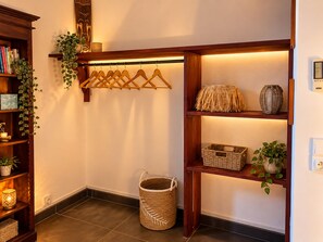 A corner of a room with a wooden shelf holding books, a hanging rack, and a basket. - Gite La Tortue Bleue (Bouillante)