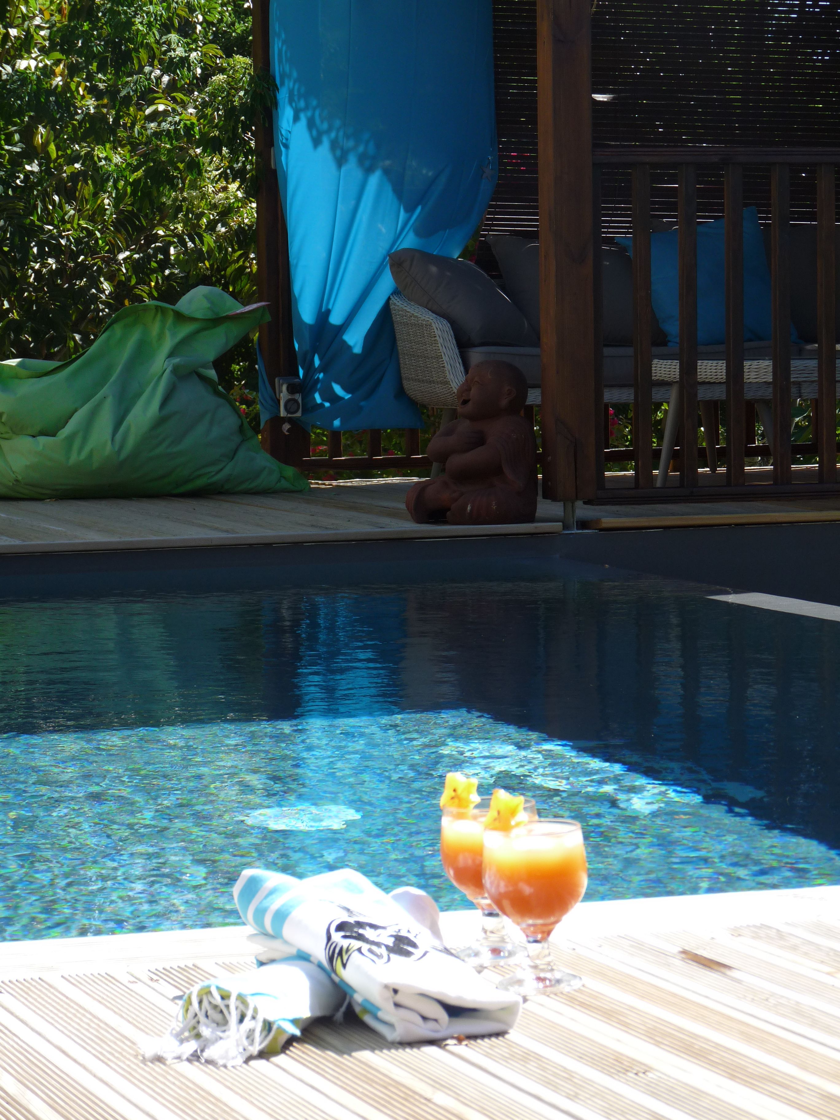 Zona junto a la piscina con una silla de descanso, una estatua de Buda infantil y una mesa con toalla y bebidas.