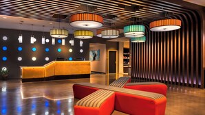 A modern hotel lobby with a reception desk, colorful pendant lights, and a seating area with red sofas. - GLō Hotel Asheville-Blue Ridge Parkway (Asheville)