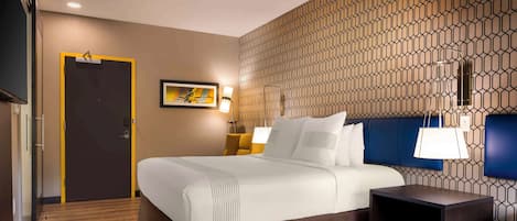 A hotel room with a bed, bedside table, lamp, and a patterned wall.