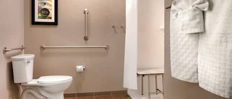 Un baño con inodoro, ducha, barra de apoyo y toallero.