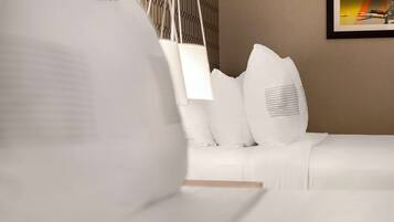 Cama bem arrumada com lençóis brancos e luminária pendente.