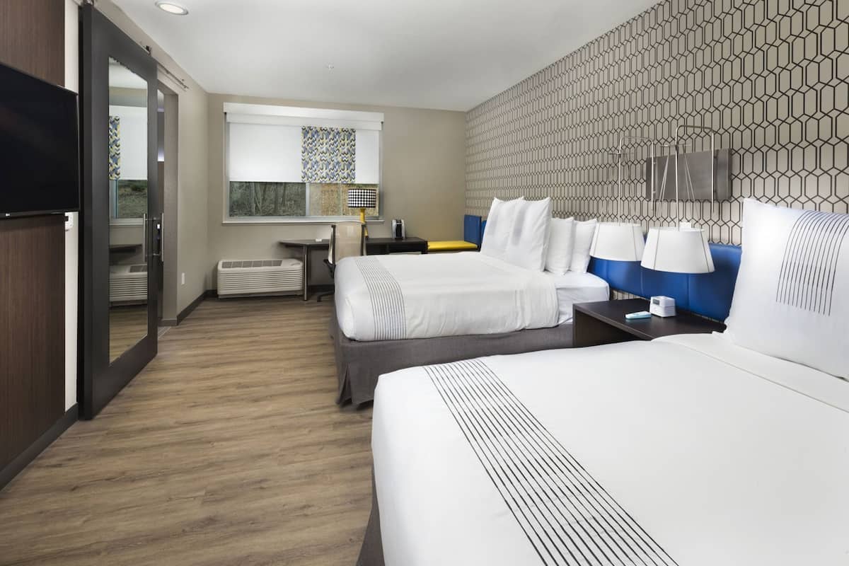 A hotel room with two beds, a desk, a chair, a window with a view, and a patterned wall.