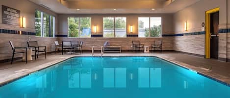 A swimming pool with chairs and tables, large windows, and a warning sign on the wall.