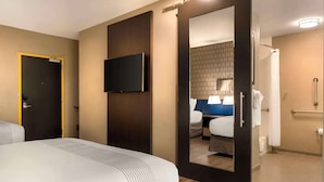 A hotel room with a bed, a TV mounted on the wall, a door leading to a bathroom, and a shower area. - GLō Hotel Asheville-Blue Ridge Parkway (Asheville)