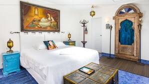Een slaapkamer met een bed, een schilderij, een houten deur en een klein tafeltje.