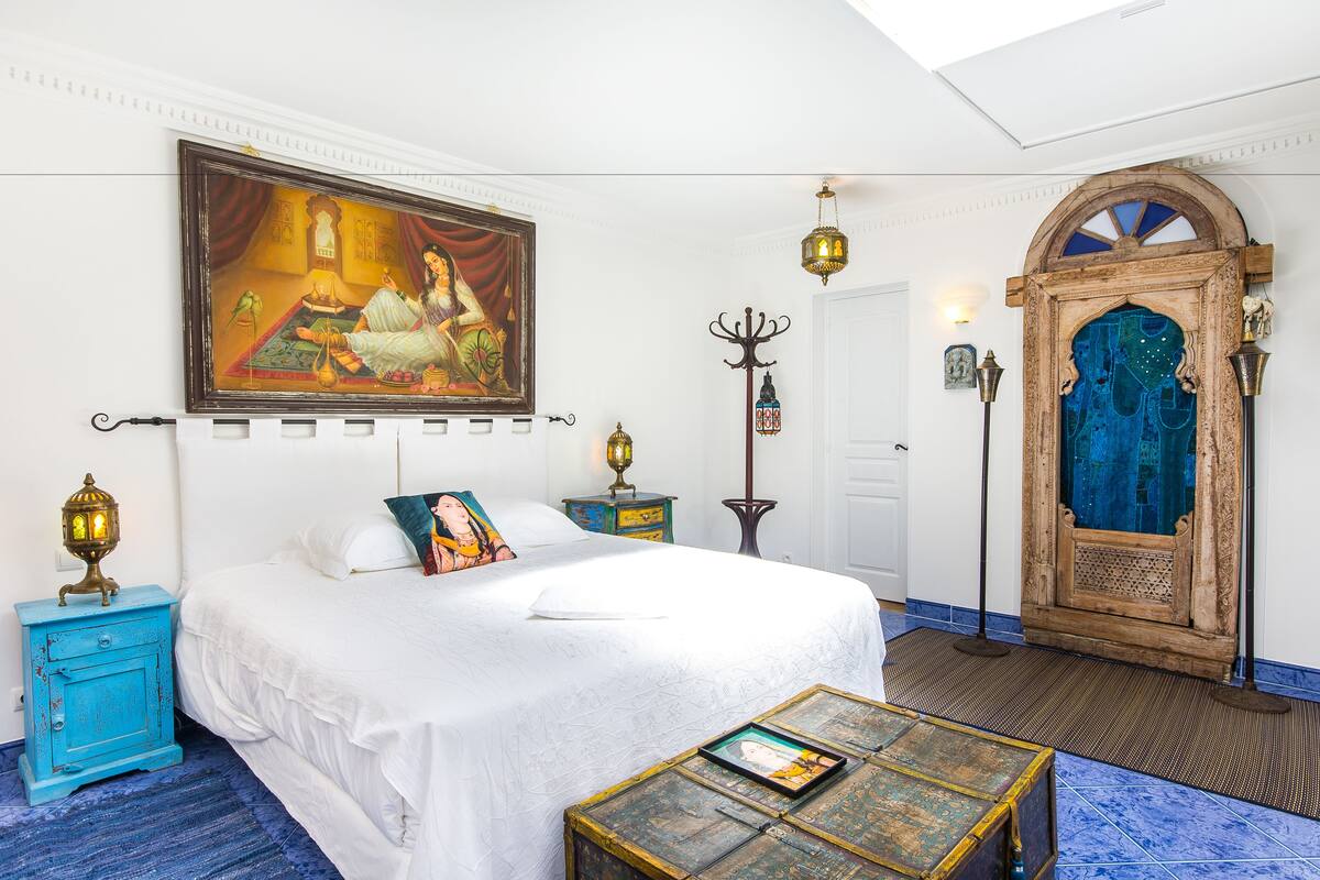 A bedroom with a bed, a painting, a wooden door, and a small table.
