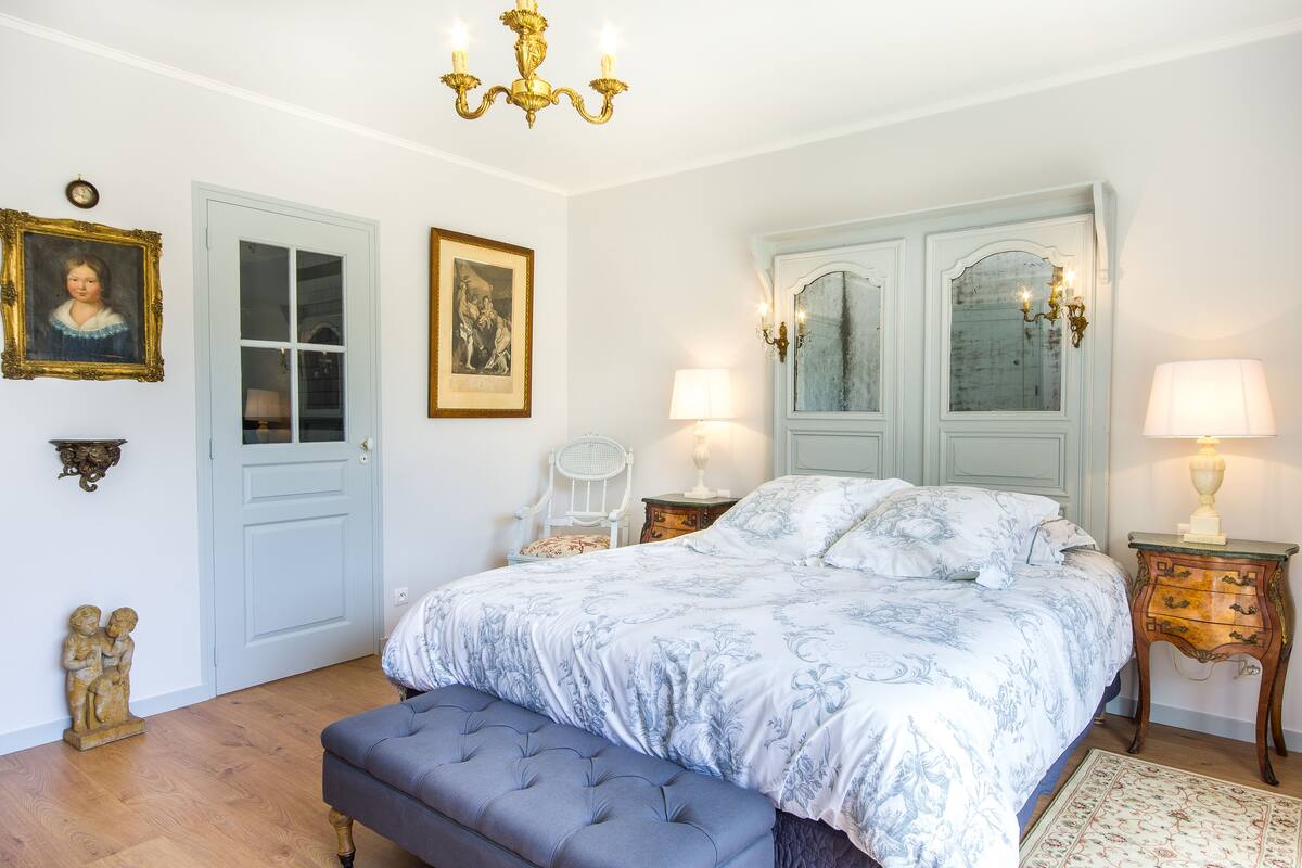 A bedroom with a large bed, two bedside tables with lamps, a chair, and a chandelier.