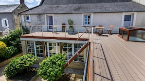 Een twee verdiepingen tellend huis met een houten terras, buitenmeubels en een glazen patio.