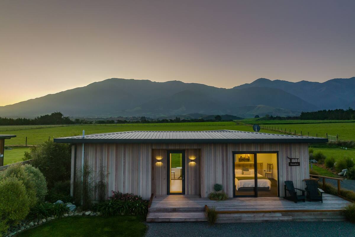 A modern cabin with a wooden exterior, a deck, and a view of mountains in the background.