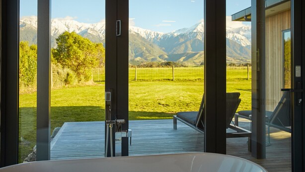 A modern room with a large window offering a view of a mountainous landscape and a grassy field. - Glenburn Coastal Retreat (Hapuku)