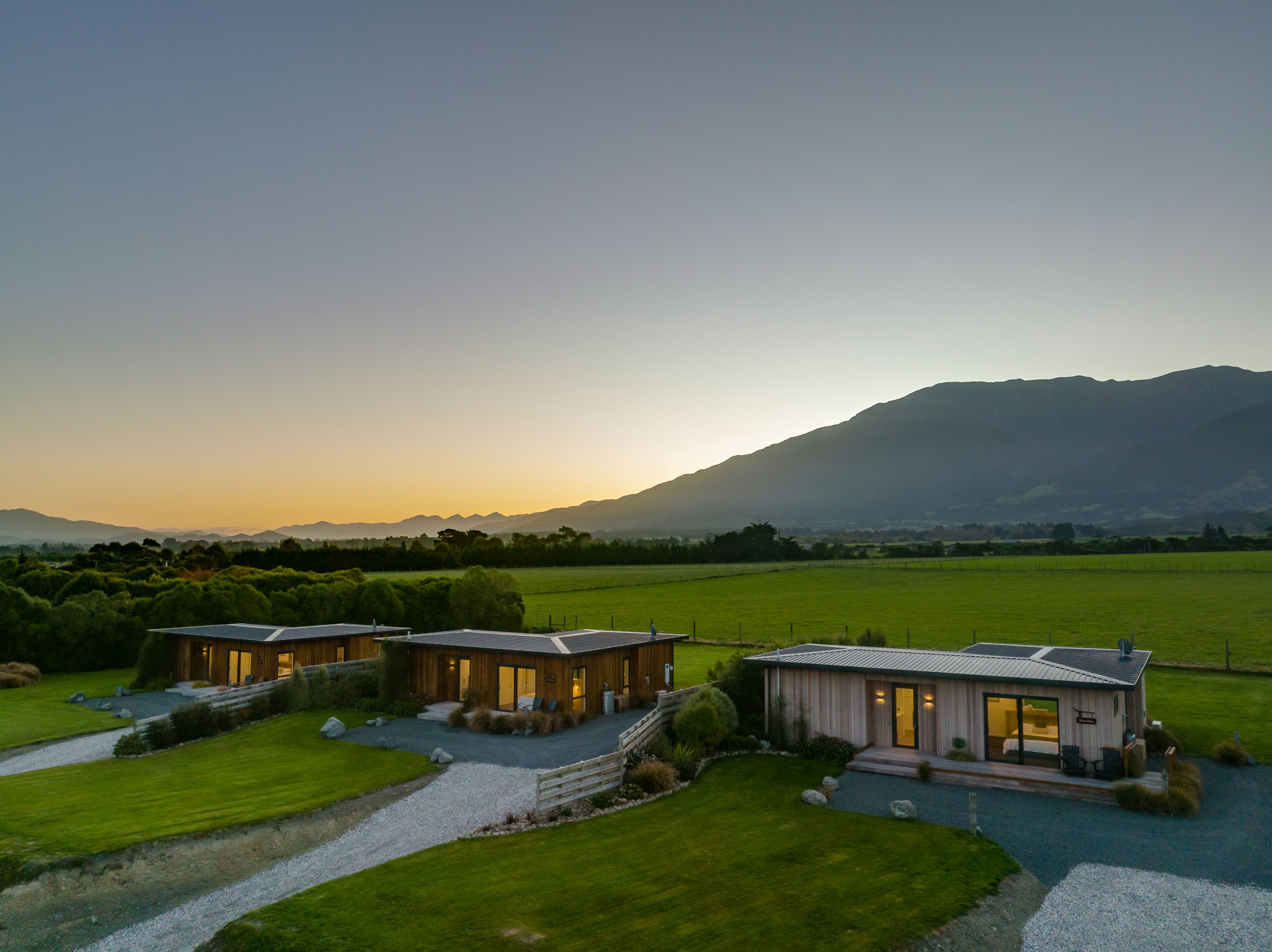 A modern two-story house with a large front lawn, a swimming pool, and a mountain backdrop.