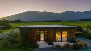A modern wooden cabin with a glass door leading to a bedroom with a bed and two chairs. - Glenburn Coastal Retreat (Hapuku)