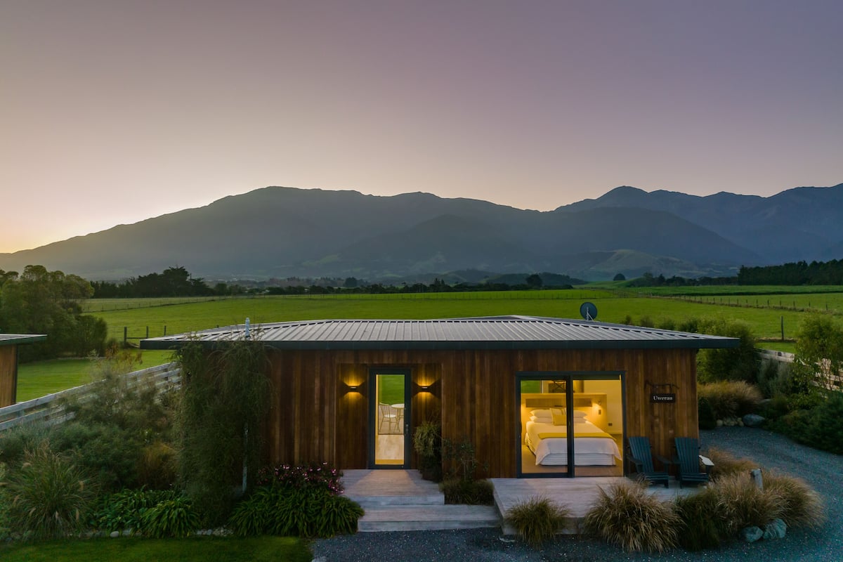 A modern wooden cabin with a glass door leading to a bedroom with a bed and two chairs.
