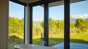 A modern bathroom with a freestanding bathtub, large windows, and a view of a mountainous landscape. - Glenburn Coastal Retreat (Hapuku)