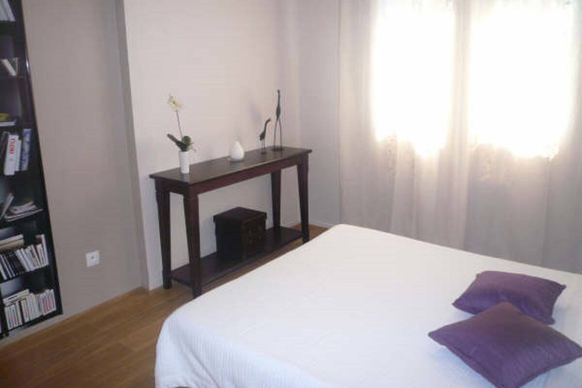 A bedroom with a bed, a bedside table, a small plant, and a bookshelf.