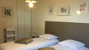 A hotel room with two beds, a bedside lamp, a shelf with towels, and artwork on the walls. - Tempologis - Meylan (Meylan)