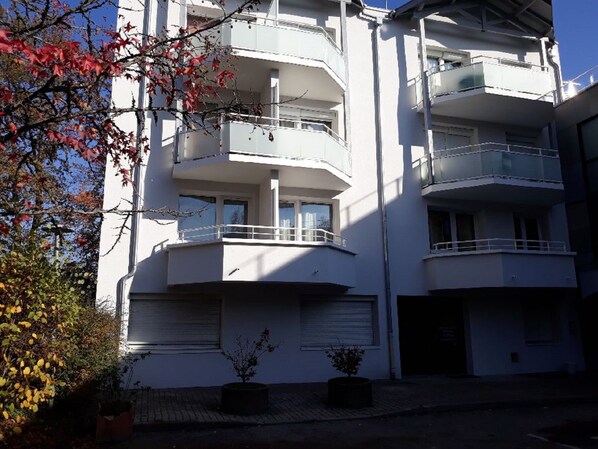 Un edificio residencial de varios pisos con balcones, un garaje y plantas en macetas.