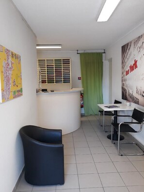 Un interior moderno con una mesa de recepción, una silla negra curvada, una mesa con sillas y una pared con nombres de ciudades.