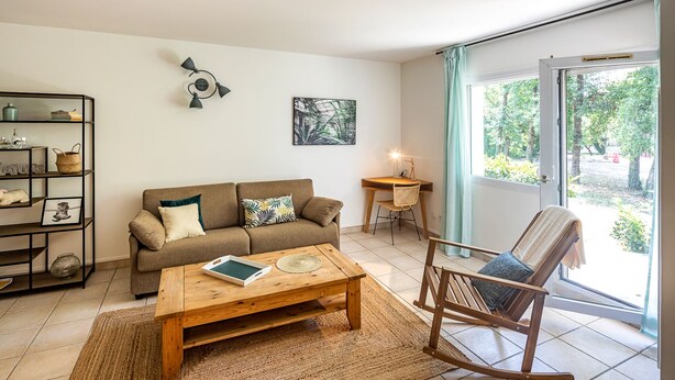 A living room with a sofa, a wooden coffee table, a rocking chair, a side table with a lamp, and a bookshelf. - Tempologis - Meylan (Meylan)