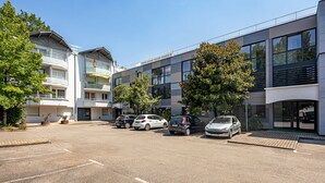 A modern building with multiple floors, a parking area with several cars, and surrounding greenery. - Tempologis - Meylan (Meylan)