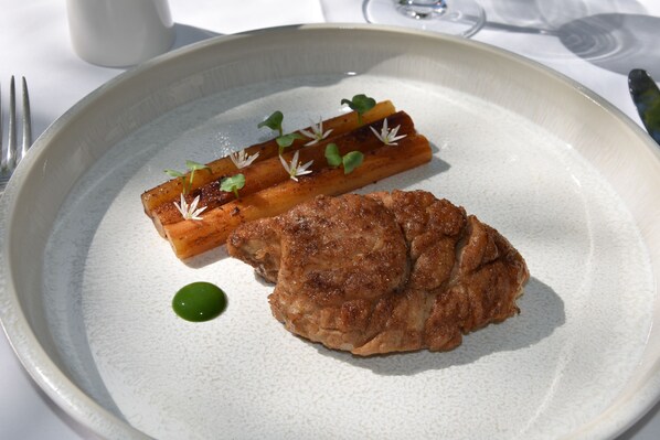A plate with a piece of meat and a vegetable garnish. - Hôtel Chavant (Bresson)