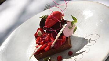 A dessert on a white plate with a chocolate base, raspberries, and a red berry on top.