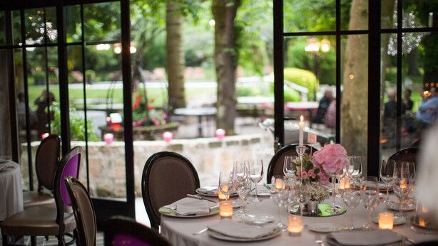A table set for dining with candles and a flower centerpiece, overlooking a garden. - Hôtel Chavant (Bresson)