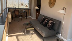 A living room with a grey sofa, two chairs, a small table, a floor lamp, and a decorative wall piece. - Hôtel Chavant (Bresson)
