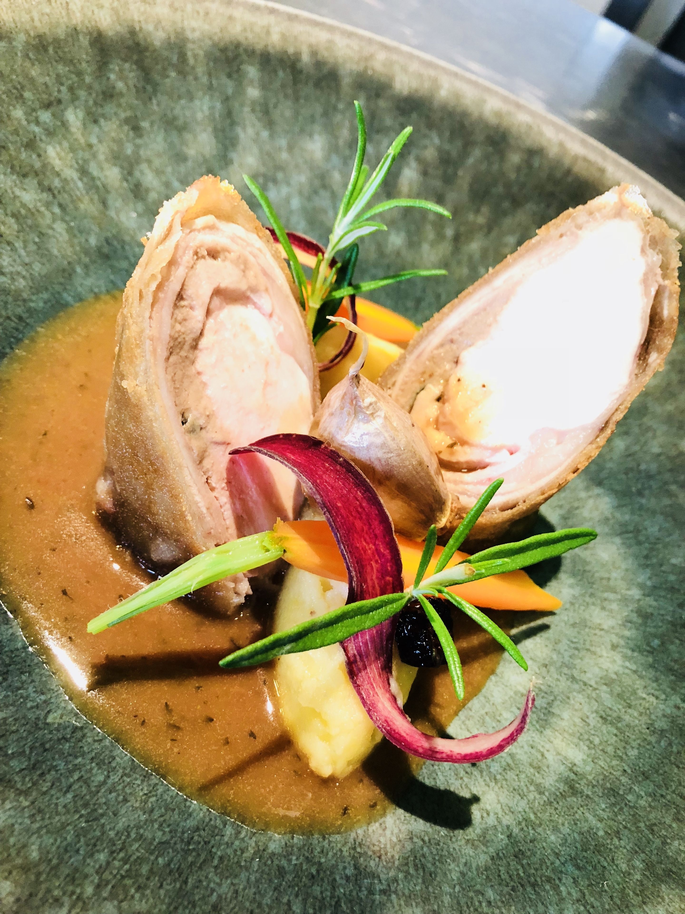 A dish with sliced meat, vegetables, and a sauce on a plate.