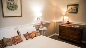 A hotel room with a neatly made bed, a small side table with a lamp, a dresser, and a framed botanical illustration on the wall. - Hôtel Chavant (Bresson)