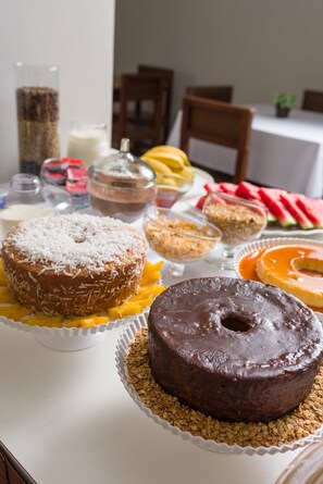 A table with various desserts including a chocolate cake, a donut, and a bowl of fruit. - Pinhal Palace Hotel (Espirito Santo Do Pinhal)
