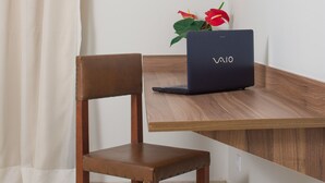 A wooden desk with a VAIO laptop, a chair, and a potted plant with red flowers. - Pinhal Palace Hotel (Espirito Santo Do Pinhal)