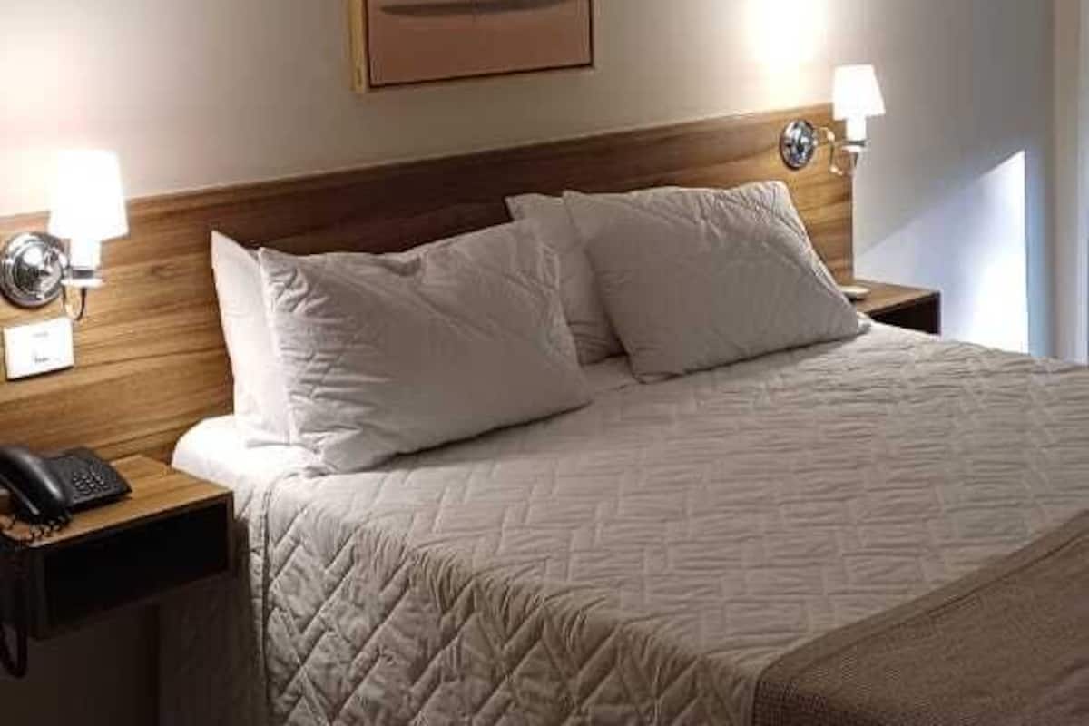 A hotel room with a bed, two bedside lamps, a nightstand with a phone, and a framed picture on the wall.