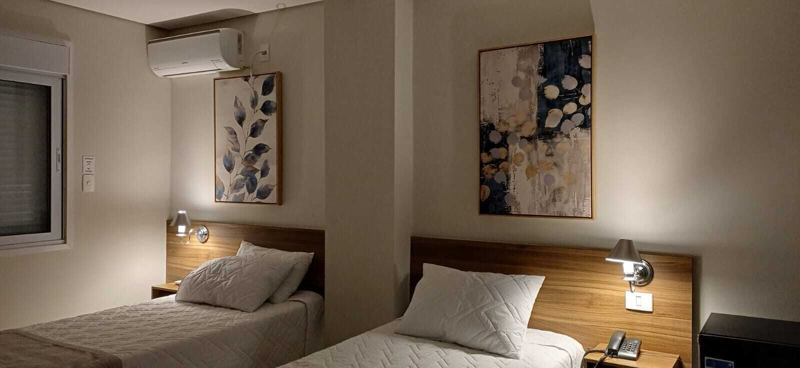 A hotel room with two beds, a wooden headboard, bedside lamps, and wall art.
