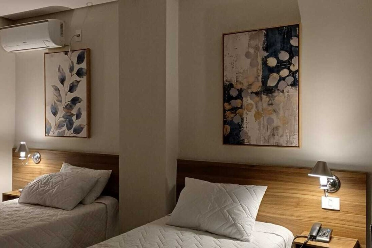 A hotel room with two beds, a wooden headboard, bedside lamps, and wall art.