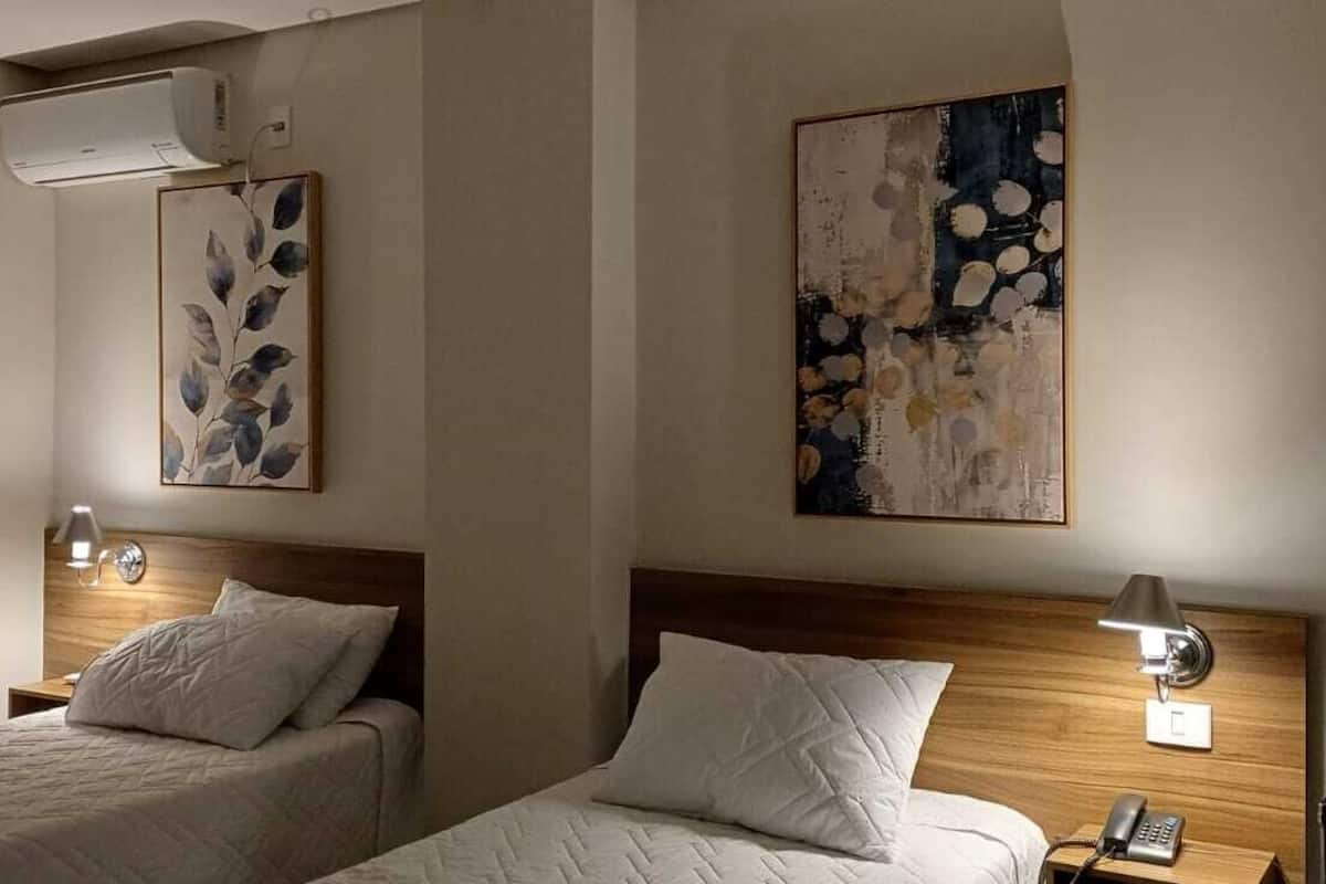 A hotel room with two beds, a wooden headboard, bedside lamps, and wall art.