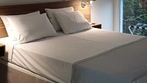 A bedroom with a bed, nightstand, lamp, and a window with blinds. - Pinhal Palace Hotel (Espirito Santo Do Pinhal)