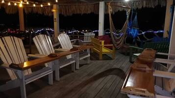 A covered outdoor seating area with wooden chairs and tables, a hammock, and string lights.