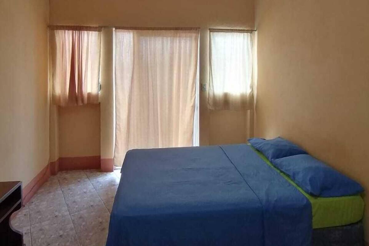 Une chambre à coucher avec un lit, des rideaux et un sol carrelé.
