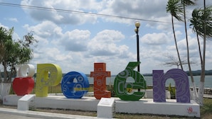 A series of colorful, abstract sculptures spelling out a word, set against a backdrop of a clear sky and palm trees. - Hotel Aurora (Flores)