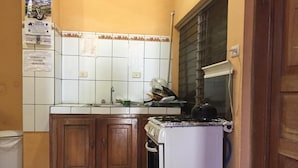 A compact kitchen with wooden cabinets, a white refrigerator, and a tiled backsplash. - Hotel Aurora (Flores)