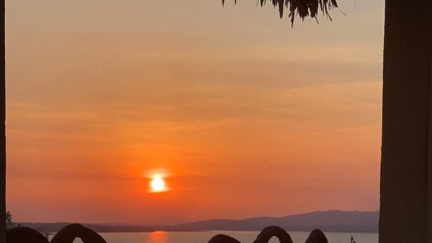 A wooden bench with a view of the sunset over a body of water, framed by a decorative arch. - Hotel Aurora (Flores)