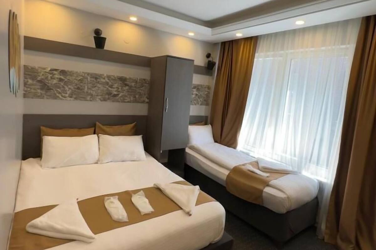 A hotel room with a large bed, a smaller bed, a wardrobe, and a window with curtains.