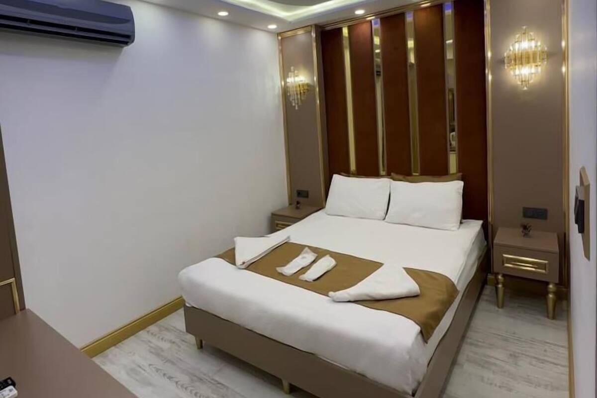 A modern hotel room with a large bed, a bedside table, a nightstand, and a wall-mounted air conditioner.